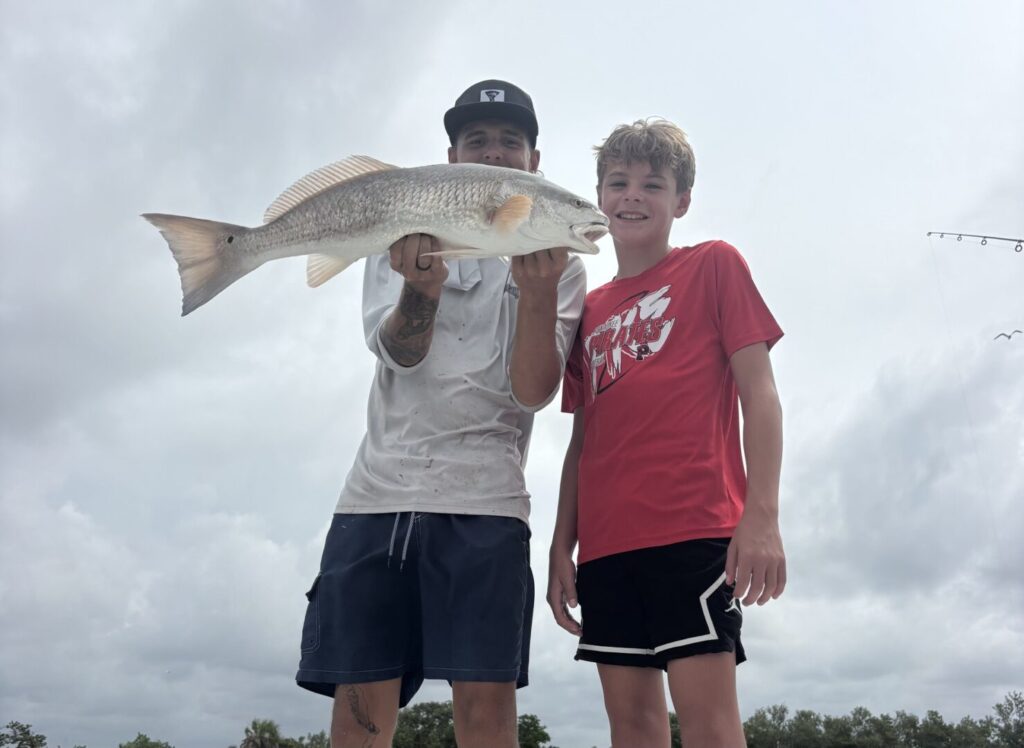 An adult and young angler holding their catch together