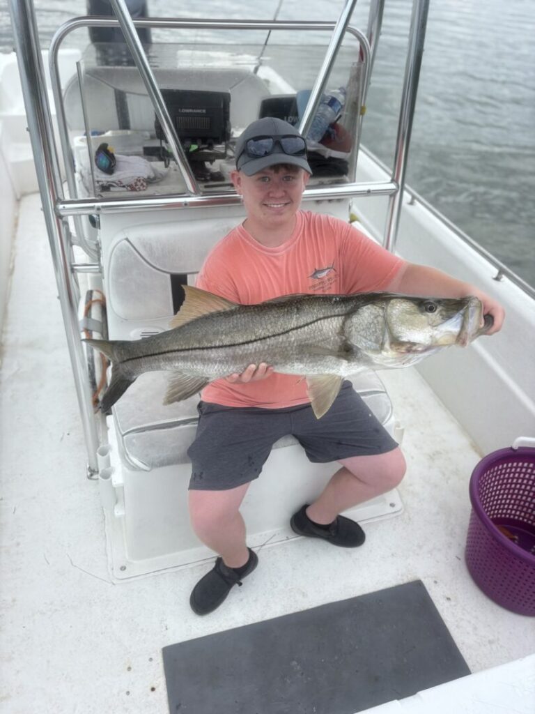 A smiling angler holding a catch while seated aboard the boat