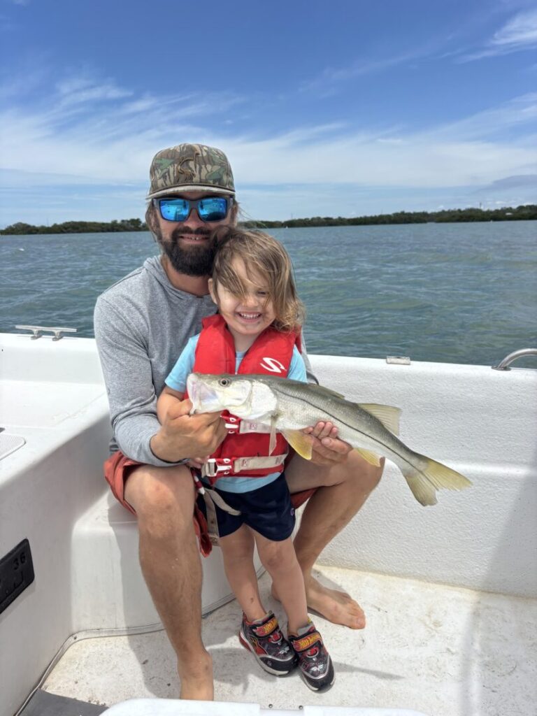 An adult and young angler holding their catch aboard the inshore boat